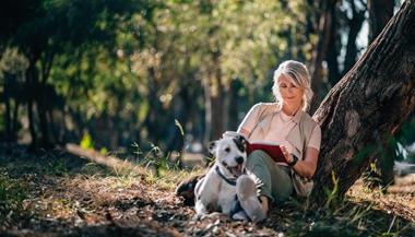 老妇人带着书和狗在森林里放松.